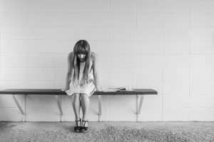 Depression - Image of a girl with head down, sitting on a bench alone
