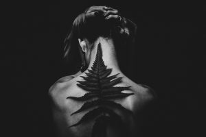 Fibromyalgia - Image of a woman's back covered with a black fern that looks like a spine, ominously